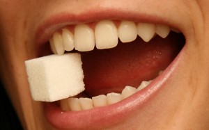 An open mouth with a sugar cube between bared teeth.