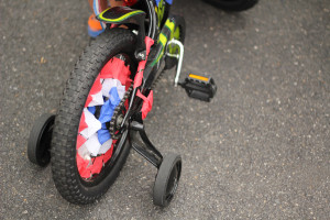 A photo of a kid's bicycle with training wheels and streamers in the main wheel.