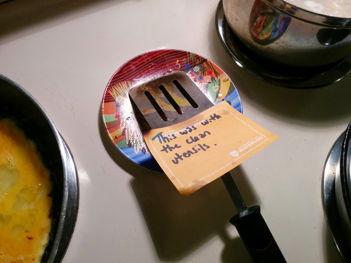 A dirty frying pan flipper, next to some pots and pans, with a note on it that reads "this was with the dirty utensils"