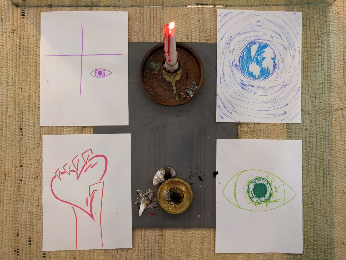 A candle surrounded by four sheets of paper. On the first is a grid with an eye in the bottom right. Below that is a hand clutching a heart. Top right is an image of the earth in space. On the bottom right is an eye with leaves and gears inside, representing eco-awareness.