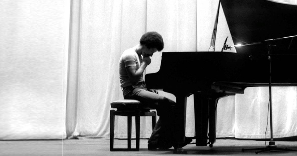 Keith Jarrett seated at a piano, looking down in reflection